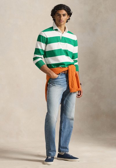 Zöld-fehér csíkos hosszú ujjú galléros ing, narancssárga pulóver a deréknál, világoskék farmer, és kék vászon tornacipő.