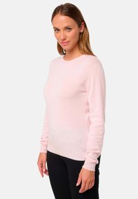 Pull en rose à manches longues en matériau doux, avec un col rond et des poignets côtelés, présentant une texture lisse et un design minimaliste.