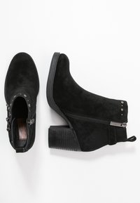 Botines de ante negros con cremallera lateral, tacón de bloque texturizado y tachuelas decorativas en el puño. Forro interior suave.