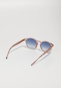 Lunettes de soleil rondes avec des verres dégradés bleu. Monture transparente rose avec des accents dorés et des branches fines et effilées. Embouts de branches texturés.