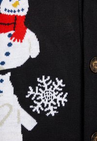 Svart stickad tröja med en vit snögubbe som har en röd scarf och blå knappar, tillsammans med ett mönster av vita snöflingor. Bruna knappar syns.