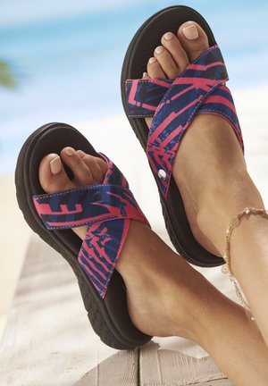 Cross-strap sandals feature a vibrant pink and blue patterned fabric upper, contrasting with a solid black rubber sole, providing lightweight comfort.