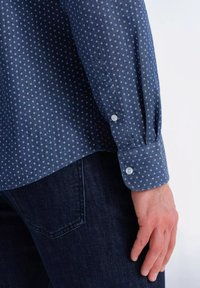 Marineblauw shirt met een klein wit ankerpatroon, lange mouwen, knoopmanchetten, gemaakt van stof met een gladde textuur, gecombineerd met donkere jeans.