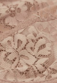 Jasnoróżowa koronkowa tkanina z misternymi wzorami kwiatowymi i teksturowanymi włóknami, z bogato zdobionymi falistymi brzegami i otwartymi splotami.