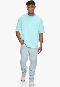 Lyseblå oversized t-skjorte med korte ermer, kombinert med lyse denimjeans og hvite joggesko med gule detaljer, med en avslappet passform.