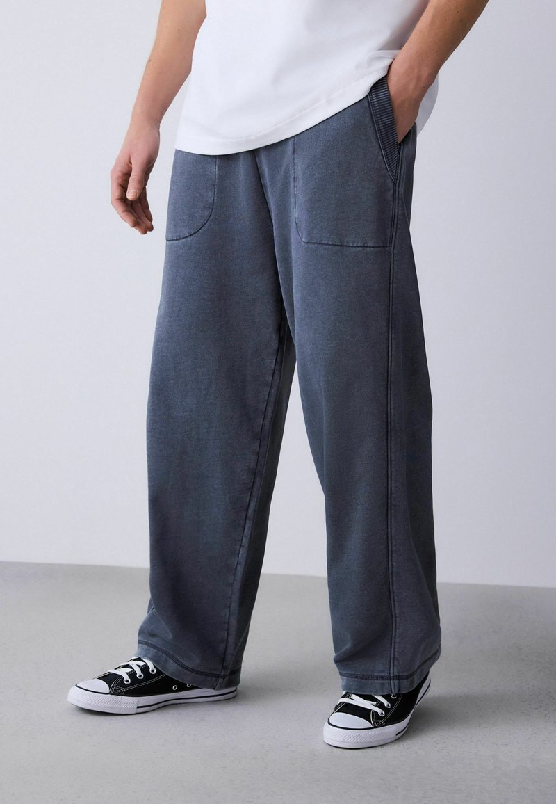 Pantaloni grigi a gamba larga realizzati in tessuto morbido con due tasche anteriori. Abbinati a sneaker basse bianche e nere.