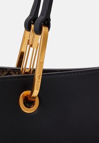 Czarna skórzana torebka z złotym metalowym zapięciem i oczkiem. Gładka tekstura z wygrawerowanym logo na zapięciu.