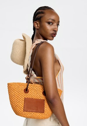 Woven orange tote bag with brown leather accents and logo. Features two handles and a spacious design. Lightweight and textured appearance.
