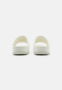 Hvite sko-sandaler med en glatt matt overflate, avrundet form, åpen bak og teksturert gummisåle. Ingen synlige logoer eller utsmykninger.