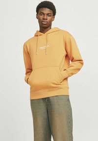 Oranje hoodie met een buidelzak en aantrekkoord. Voorzien van witte "Original Studio" tekst op de borst. Zacht materiaal en relaxed fit.