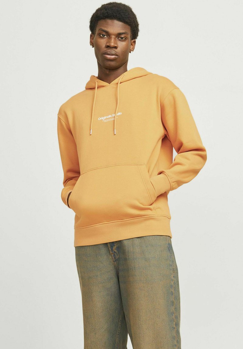 Oranje hoodie met een buidelzak en aantrekkoord. Voorzien van witte "Original Studio" tekst op de borst. Zacht materiaal en relaxed fit.