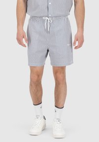 Stripete shorts i blått og hvitt, elastisk midje med snor, sidelommer, brukt med hvite sneakers og ankelsokker.