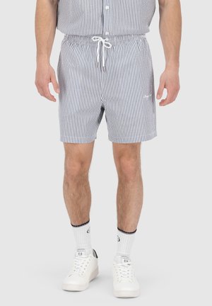 Shorts rayés en bleu et blanc, taille élastique avec cordon de serrage, poches latérales, portés avec des baskets blanches et des chaussettes mi-mollet.