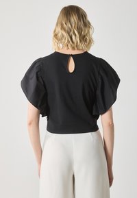 Black cropped top featuring puff sleeves and a keyhole back detail, made from soft fabric with a smooth texture, paired with light-colored pants.