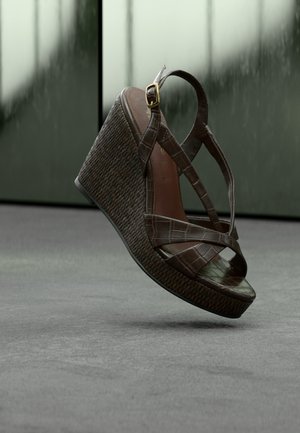 Brown wedge sandal with crisscross straps made of textured leather. Features a patterned woven heel and golden buckle detail.