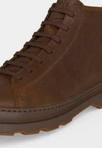 Chaussure montante en cuir marron avec lacets assortis, coutures apparentes et semelle en caoutchouc robuste avec relief, adaptée pour une utilisation extérieure.