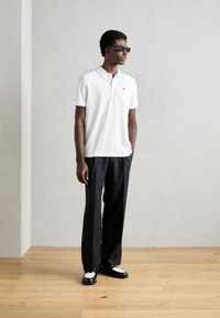 Hvit polo skjorte med krage, brukt med svarte bukser. Svart og hvite loafers. Mannlig figur står mot en nøytral bakgrunn.