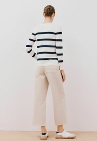 Maglione a righe, blu navy e bianco, con maniche lunghe. Pantaloni ampi beige. Sneakers bianche con dettagli neri sul tallone. Sfondo neutro.
