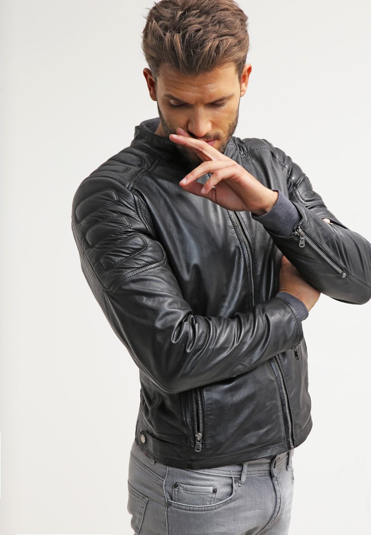 Chaqueta de cuero negra con parches acolchados en los hombros, bolsillos con cremallera y un diseño ajustado. Top de manga larga gris visible debajo.