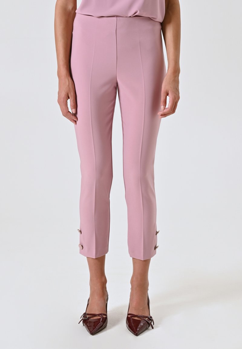 Pantaloni rosa su misura con una texture liscia, lunghezza cropped e dettagli con bottoni all'orlo. Indossati con tacchi a punta bordeaux.