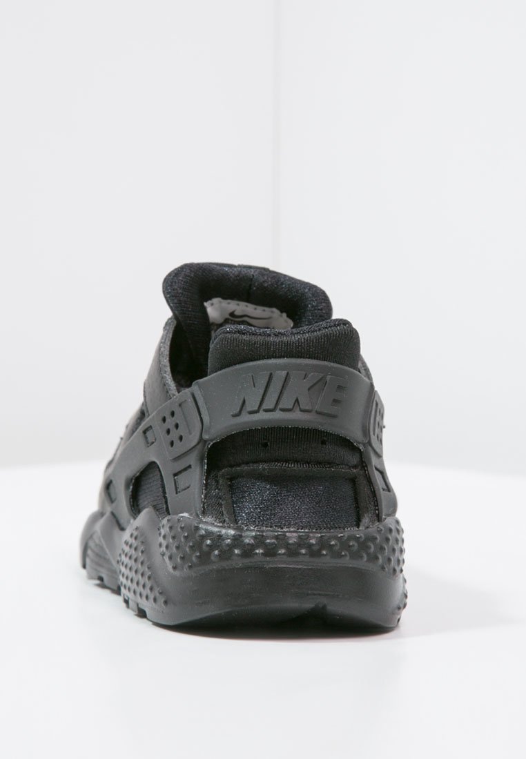 Zapatilla deportiva negra con suela de goma texturizada, parte superior de malla y detalles perforados. Cuenta con un talón acolchado y un destacado logo de Nike.