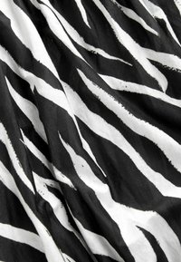 Tissu noir et blanc avec un motif de rayures zébrées ondulées et des plis visibles créant texture et ombres.