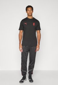 Sort kortærmet t-shirt med rødt logo, parret med sorte sweatpants med røde accenter og sidelægning, fuldendt med sportssko.