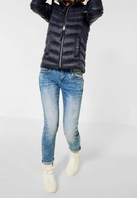 Marinblå pufferjacka med horisontellt quiltat mönster, dragkedja och vit foder; matchad med ljusblå slim fit jeans och vita sneakers.