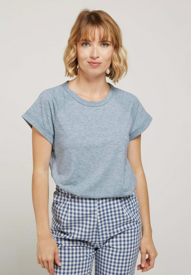 T-shirt bleu chiné avec un col rond et des manches courtes roulées, associé à un pantalon à carreaux bleu et blanc. Texture de tissu douce.