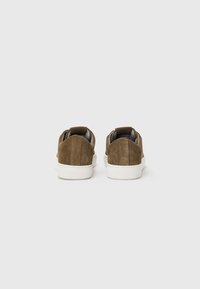 Tênis de camurça castanho com sola de borracha branca e puxadores no calcanhar, apresentando um design suave e minimalista para uso casual.