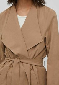 Sandfärgad omlottskappa med bred krage, bälte och framfickor. Tillverkad av mjukt tyg, har en strukturerad yta och en figurnära silhuett.