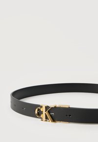 Μαύρη δερμάτινη ζώνη με αγκράφα λογότυπου "cK" σε χρυσό, τοποθετημένη επίπεδα σε λευκή επιφάνεια.