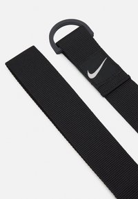 Musta nailonihihna, jossa on teksturoidun pinnan, pyöreä muovilenkki ja pieni Nike-logopatch. Yksinkertainen muotoilu korostaa toiminnallisuutta.