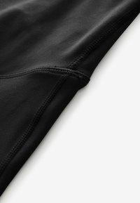 Schwarzes Kleidungsstück aus glattem, dehnbarem Material. Verfügt über sichtbare Nähte und ein eng anliegendes Design, das eine stromlinienförmige Silhouette betont.