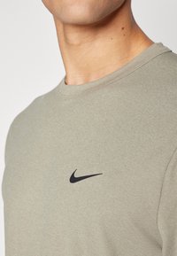 Heled oliivroheline puuvillane T-särk ringkaeluse ja lühikeste varrukatega, millel on must Nike'i sird logo rinnal.