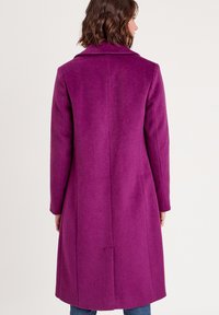 Manteau en mélange de laine violet avec une silhouette longue, un col en notch et une texture lisse. Présente une fente au dos et une coupe ajustée.