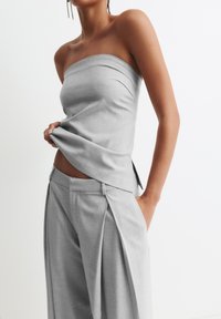 Grauer trägerloser Top aus glattem Stoff, kombiniert mit taillierten grauen Hosen mit Falten und seitlichen Taschen, die ein elegantes Profil zeigen.