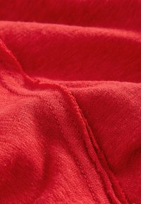 Tissu rouge avec une surface douce et texturée, présentant des variations subtiles de teinte et des détails de fine couture le long des bords.