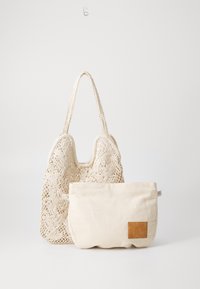 Sac cabas crème tissé avec un motif en dentelle florale et deux poignées, accompagné d'une pochette en tissu beige avec un accent en cuir marron.