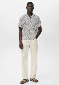 Camisa de manga corta con un patrón geométrico en blanco y negro, combinada con pantalones de color claro y sandalias marrones.