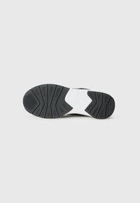 La suola della sneaker nera in gomma presenta un motivo testurizzato con un accento bianco, progettata per la trazione e il comfort.