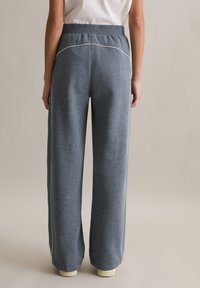 Szare spodnie dresowe o szerokich nogawkach, wykonane z miękkiego materiału, z prążkowanym paskiem w talii i białym przeszyciem wzdłuż szwów. Manżety mają prążkowane wykończenie.