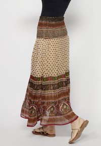 Long, flowy skirt with a smocked, patterned waist. Features a light, sheer fabric with floral and geometric designs in earthy tones.