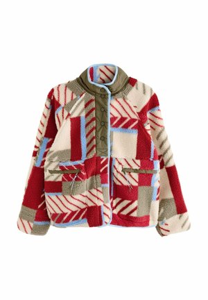 Personne portant une veste polaire à motifs rouge, beige et bleu sur un top blanc court et un jean taille haute bleu clair.