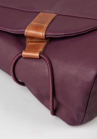 Paarse stoffen tas met een gladde textuur, voorzien van een bruin leren accent en een bungeekoordsluiting aan de voorkant.