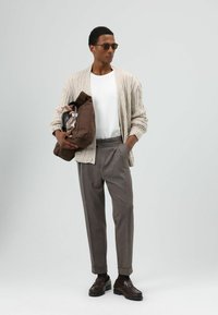 Gebreide beige cardigan over een wit T-shirt, grijze geplooide broek, bruine loafers, met een bruine tas en een sjaal met patroon.