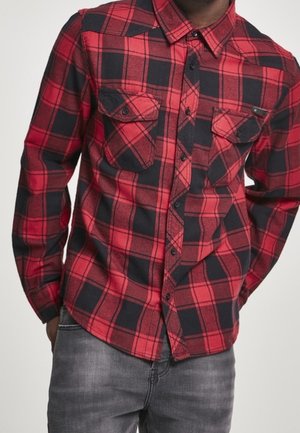 Chemise en flanelle à carreaux rouges et noirs avec des manches longues, un col pointu et deux poches poitrine. Boutons visibles sur le devant.