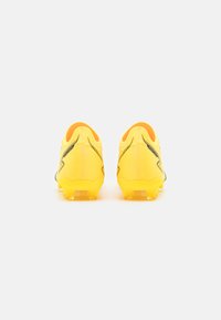 Botas de fútbol amarillas con una superficie texturada, acentos negros y una forma aerodinámica. Clavos visibles en la suela para tracción.