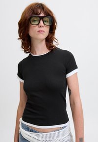 Black fitted t-shirt with white trim on sleeves and neckline. Model wears oversized dark sunglasses. Background is plain and light.