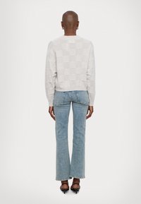 Maglione grigio chiaro lavorato a maglia con texture a quadri, abbinato a jeans flare azzurri a vita alta e sandali neri con tacco.
